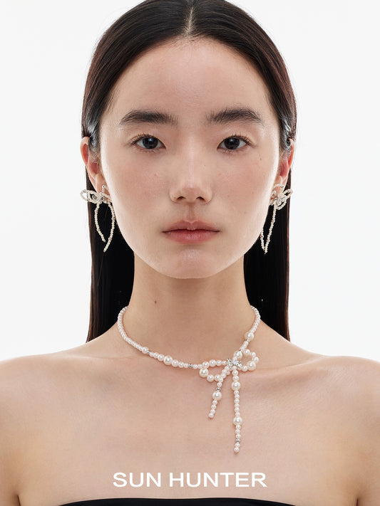 Elegant SUN HUNTER pearl bow ribbon earrings showcased on a model's ears with a simple background