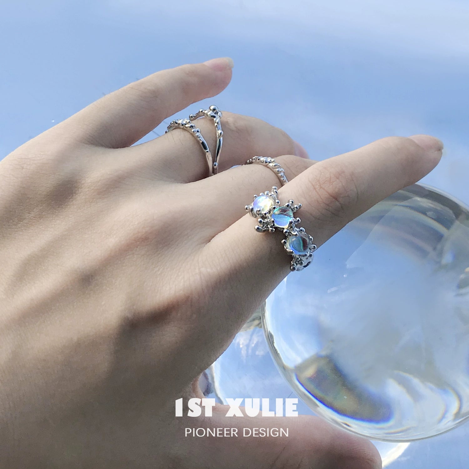 Beautiful moonstone silver ring displayed on a hand with other silver rings in a serene setting