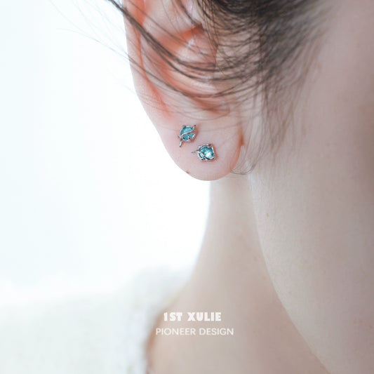 Elegant ocean blue stud earrings displayed on a model's ear, showcasing their shimmering design