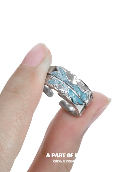 Azure dream fish ring with intricate wave design held between fingers for a unique ocean-inspired look