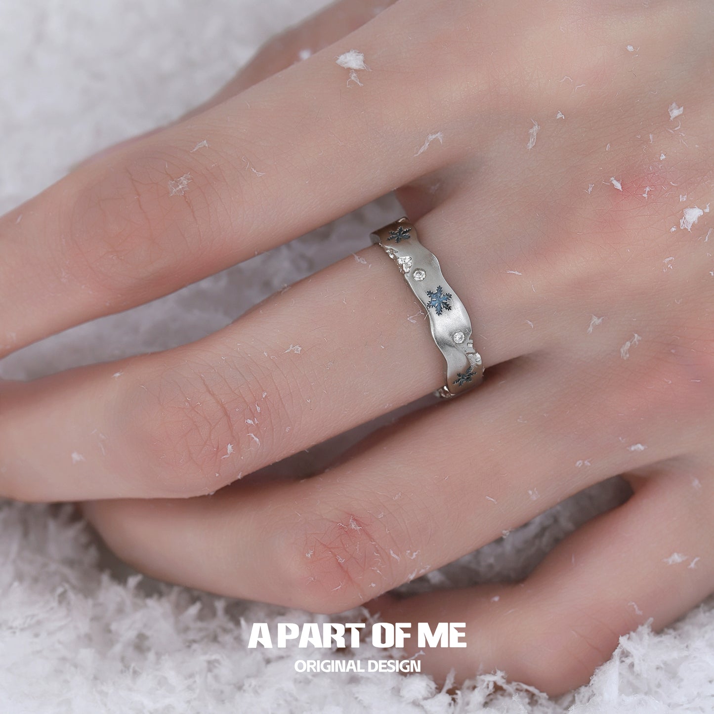 A silver snowflake love ring with delicate blue accents showcased on a hand in snow