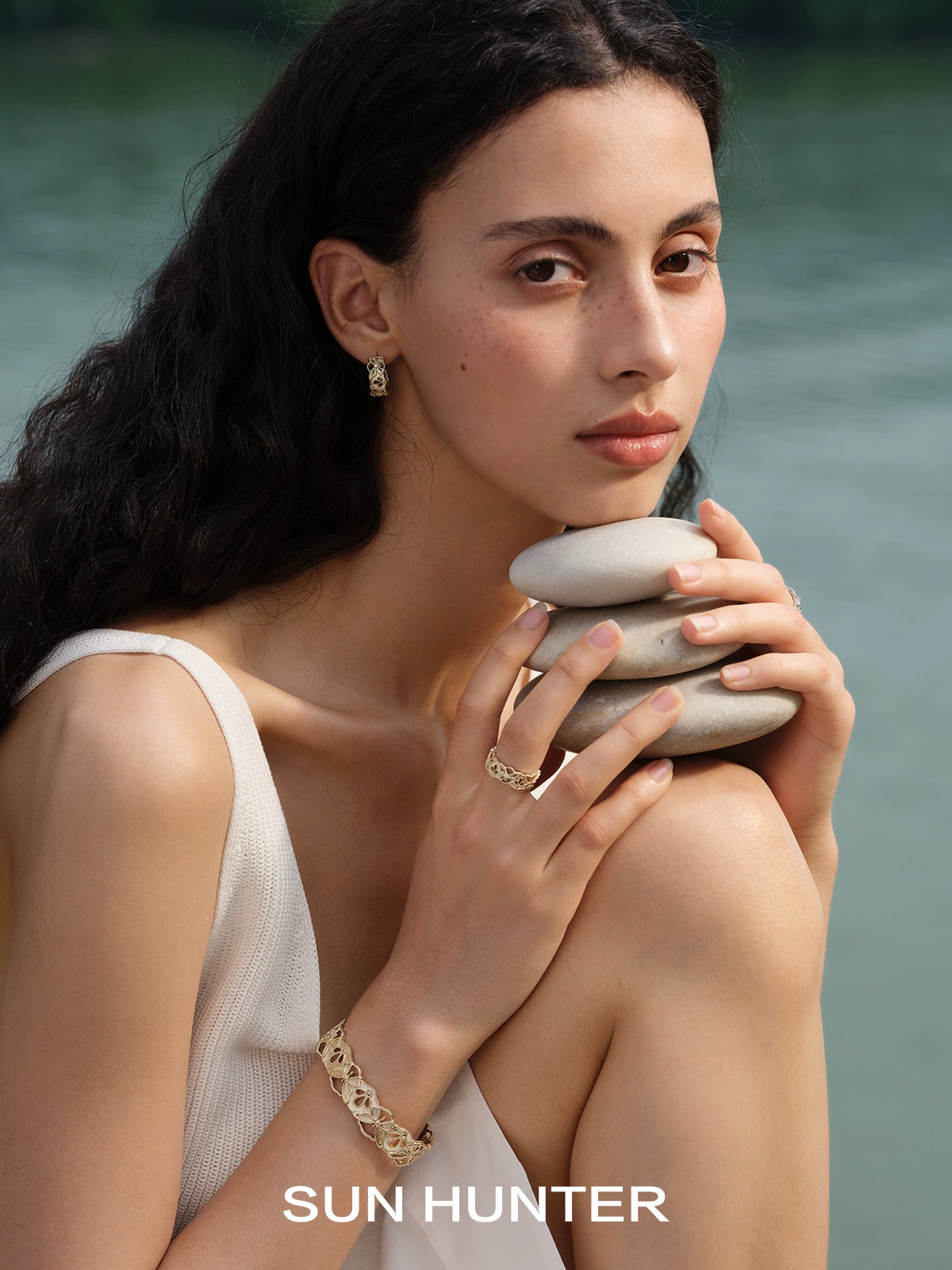 Elegant SUN HUNTER butterfly hollow ring worn by a model holding smooth stones by the water
