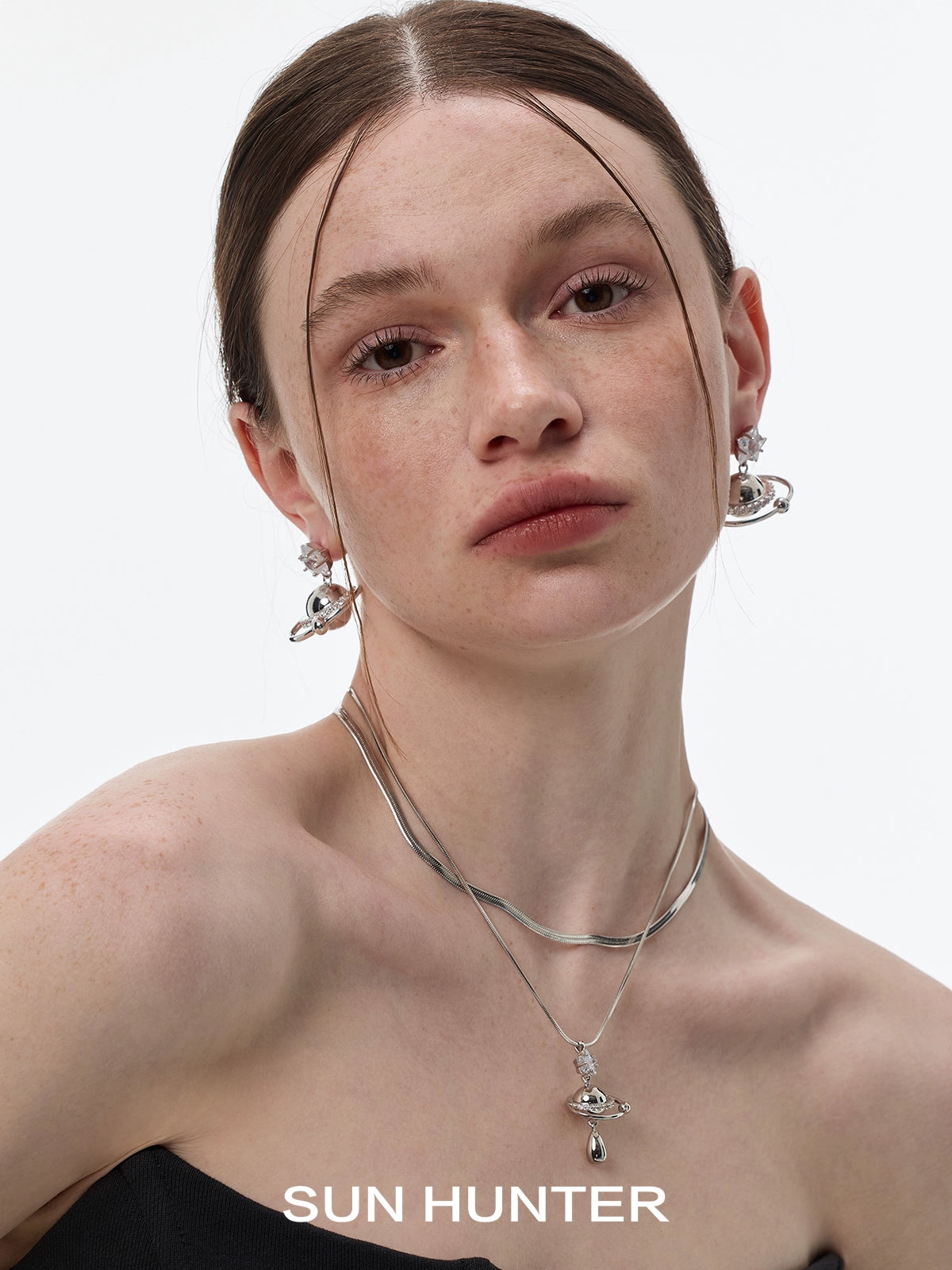 Model wearing SUN HUNTER cosmic planet star earrings with a stylish silver necklace
