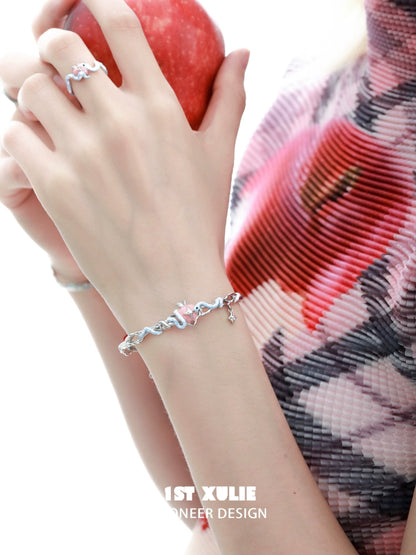 Cute snake apple bracelet in silver worn on a hand holding a red apple, perfect for trendy accessories
