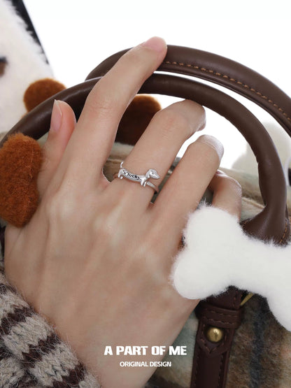 Silver dachshund silver ring worn on a hand holding a stylish handbag with dog bone accessories