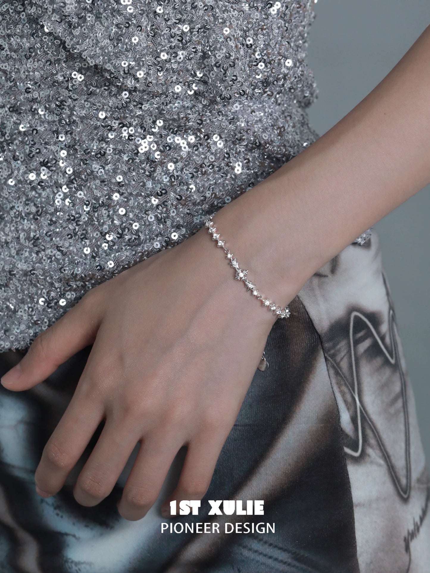 Stylish four-point star silver bracelet worn on a hand with a sparkling outfit