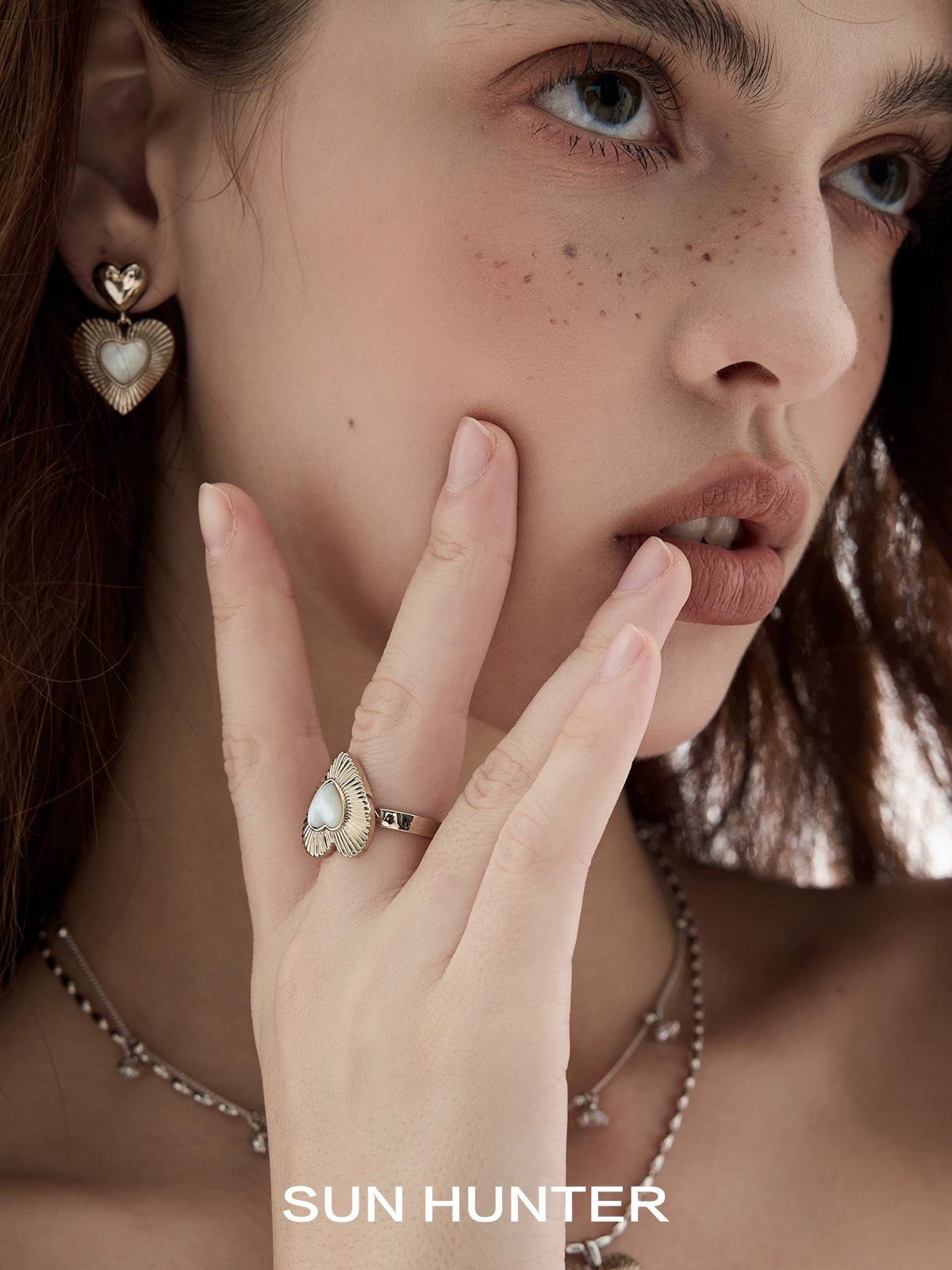 Fashion model wearing SUN HUNTER heart shaped statement earrings with a matching ring and delicate chain necklace