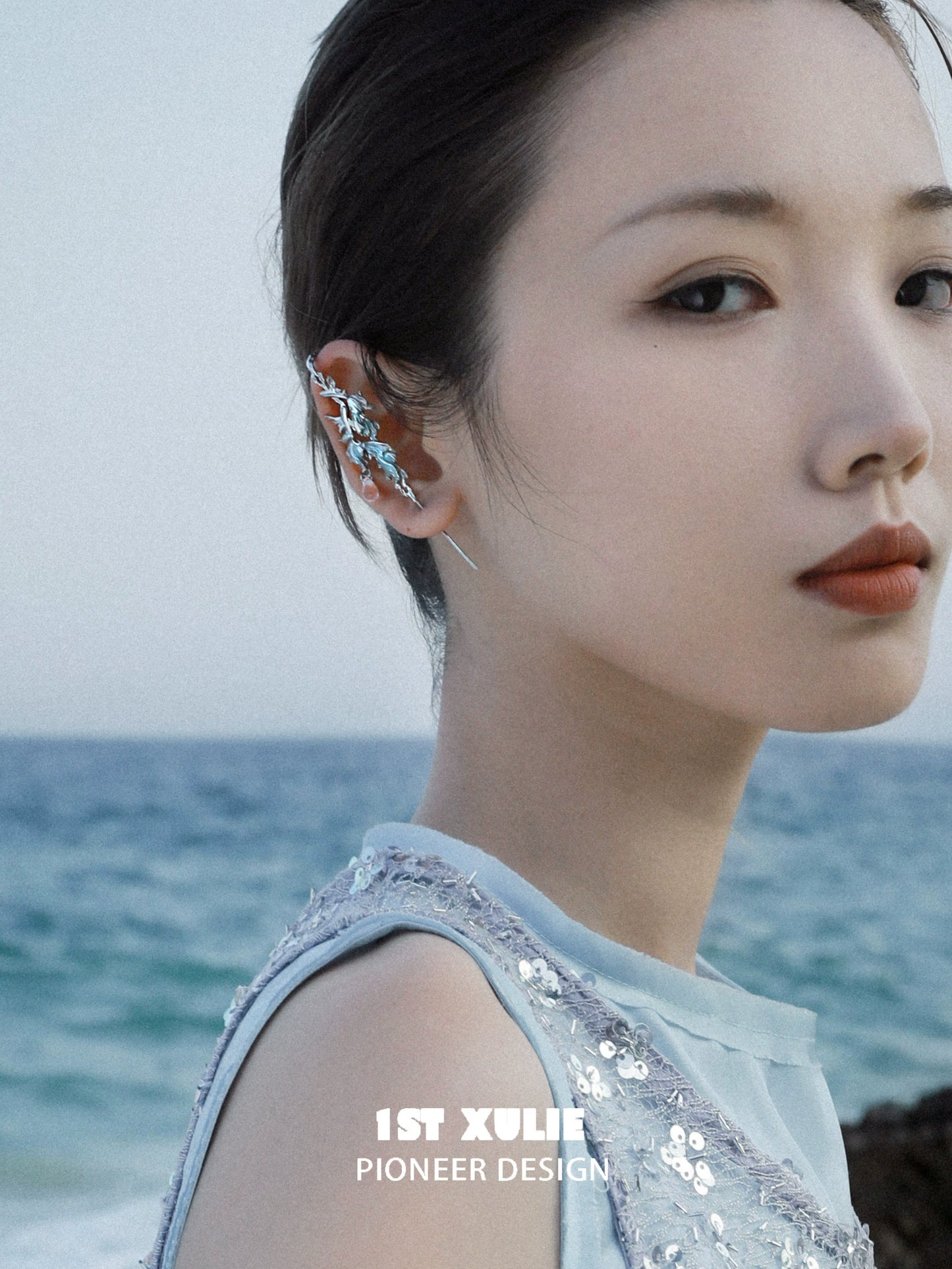 Stylish mermaid tail ear piercing jewelry showcased on a model by 1STXULIE near the ocean