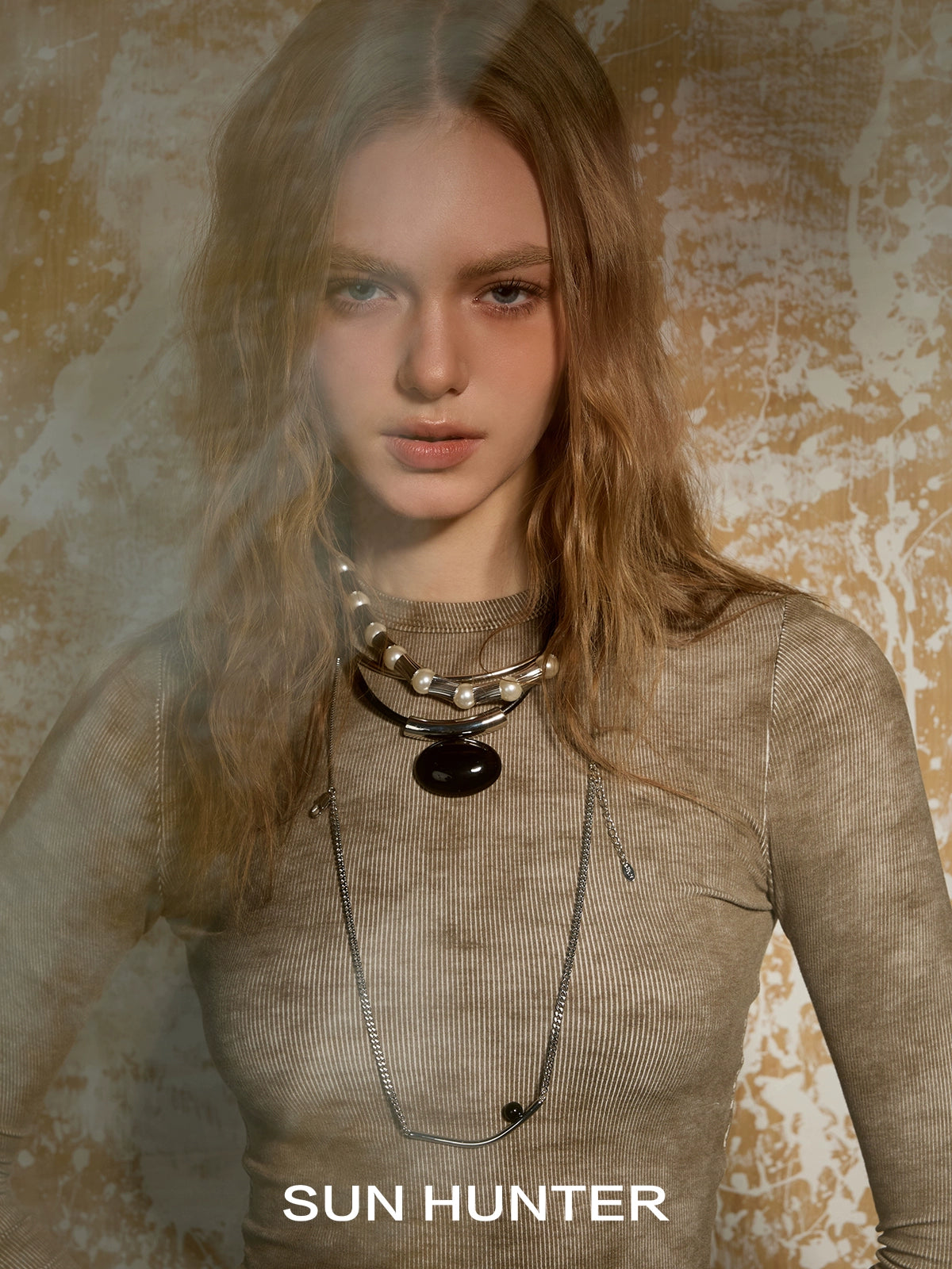 Model wearing SUN HUNTER molten drop necklace layered with pearls and silver chains