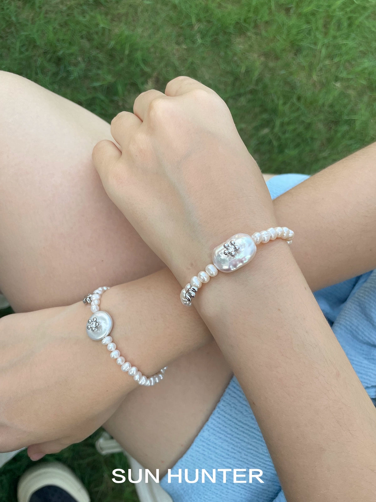 Two SUN HUNTER ocean memory pearl bracelets with elegant designs worn on wrists in a natural setting