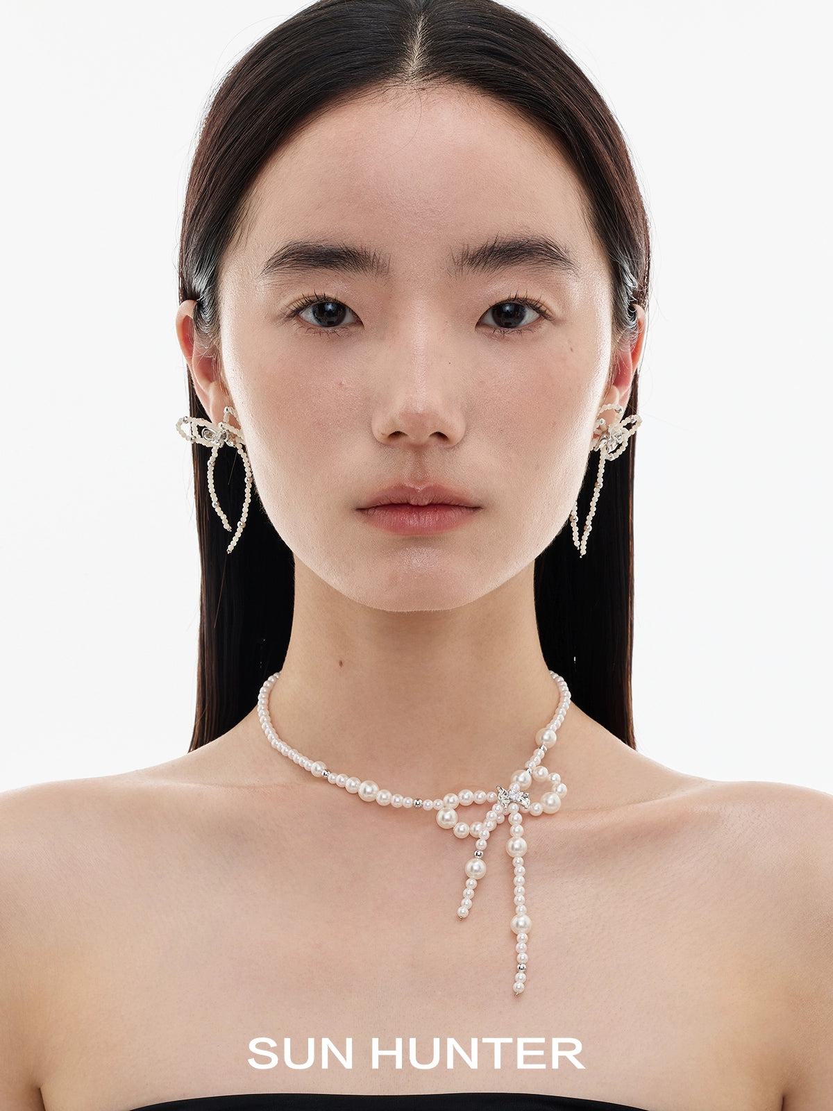 Elegant SUN HUNTER pearl bow ribbon earrings showcased on a model's ears with a simple background