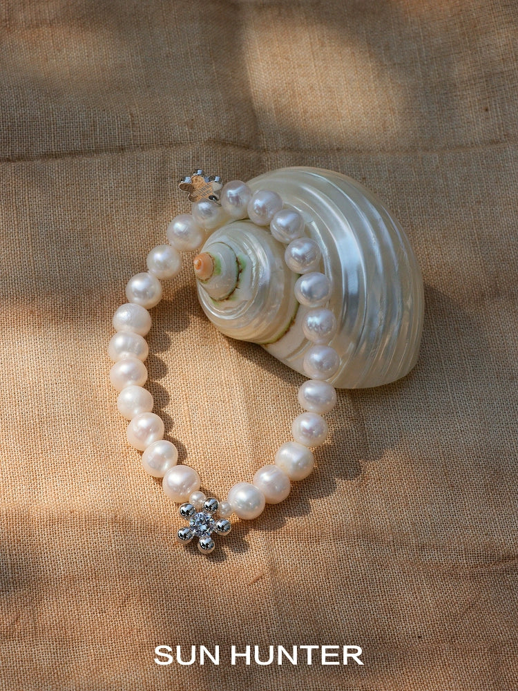 Elegant pearl bracelet for women featuring a sparkling floral clasp, displayed on a seashell