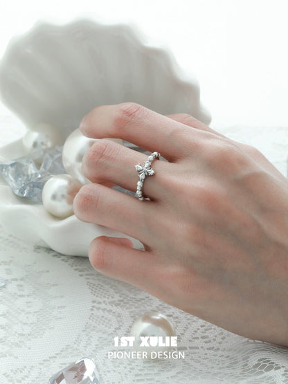 Elegant pearl cross silver ring displayed on a hand with a decorative shell and pearls in the background