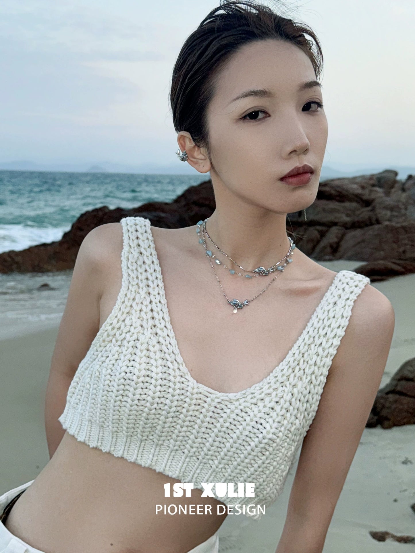 Model wearing a stylish playful fish necklace paired with a white knitted crop top at the beach