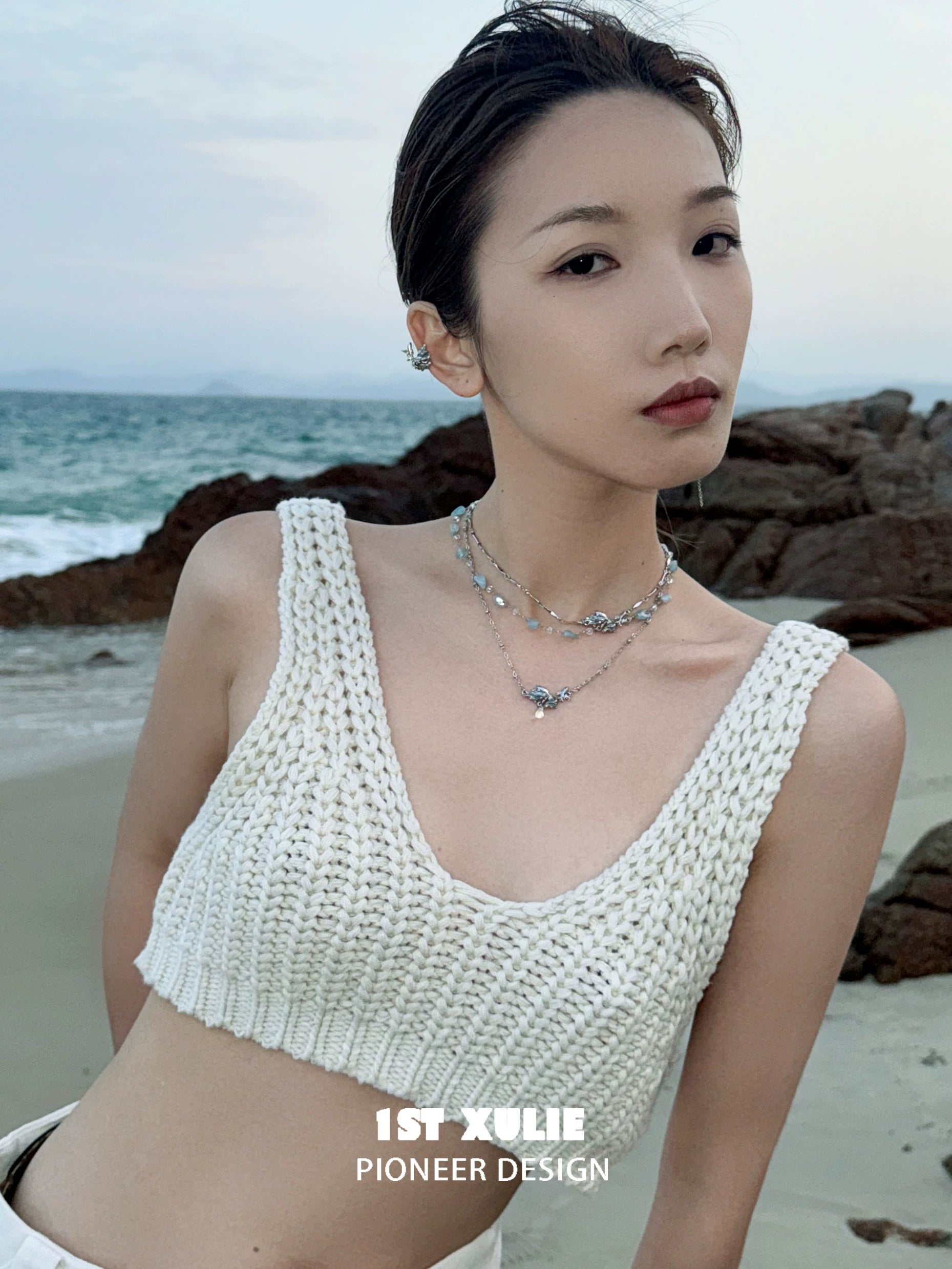 Model wearing a stylish playful fish necklace paired with a white knitted crop top at the beach