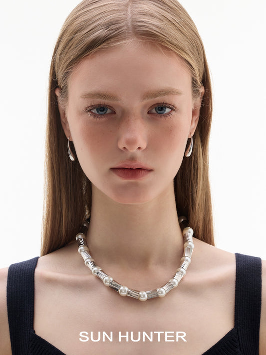 Model wearing SUN HUNTER retro metal water drop earrings with a pearl necklace, showcasing a stylish look