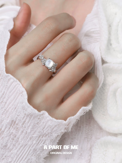 A PART OF ME rose silver ring with a large stone and decorative details worn on a hand with a white sweater