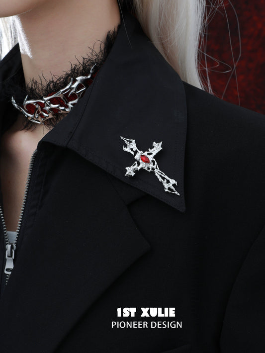 Sacred cross silver brooch adorned with red jewel on a black jacket collar