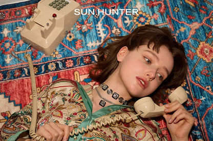 Model wearing a retro coin ring while lying on a colorful rug with a vintage telephone