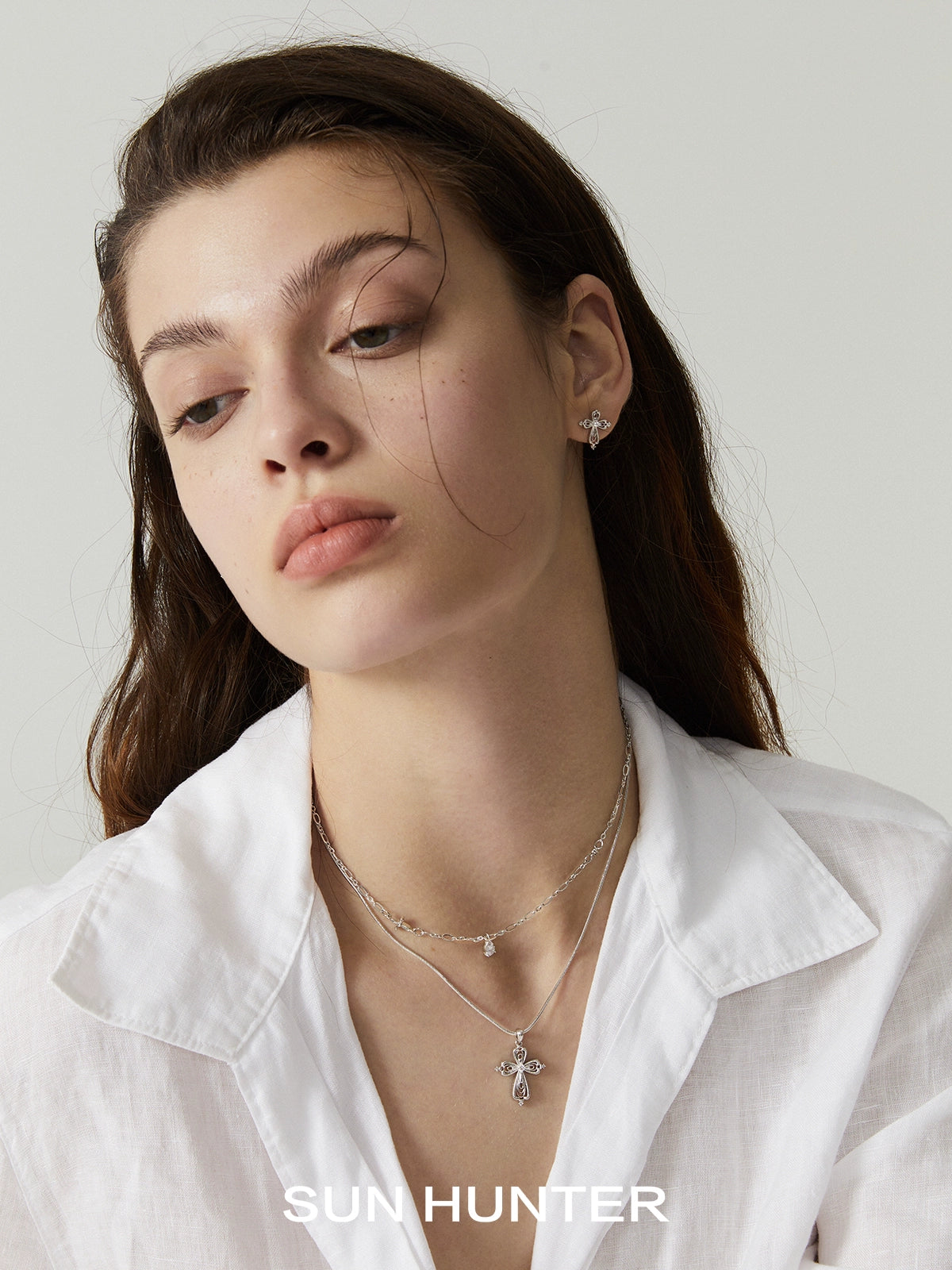 Model wearing a silver teardrop cross necklace layered with delicate jewelry
