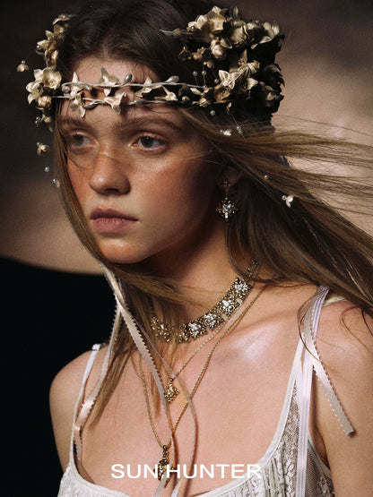 Model wearing unique floral drop earrings from SUN HUNTER with a floral crown and layered necklaces
