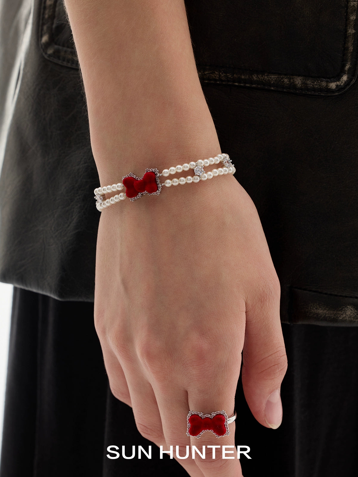 Sun Hunter velvet bow pearl bracelet displayed on a model's wrist, featuring a striking red bow design