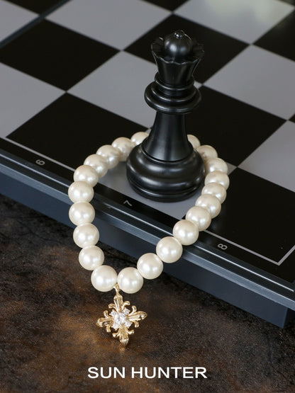 SUN HUNTER vintage iris pearl bracelet with a gold floral charm next to a chess piece
