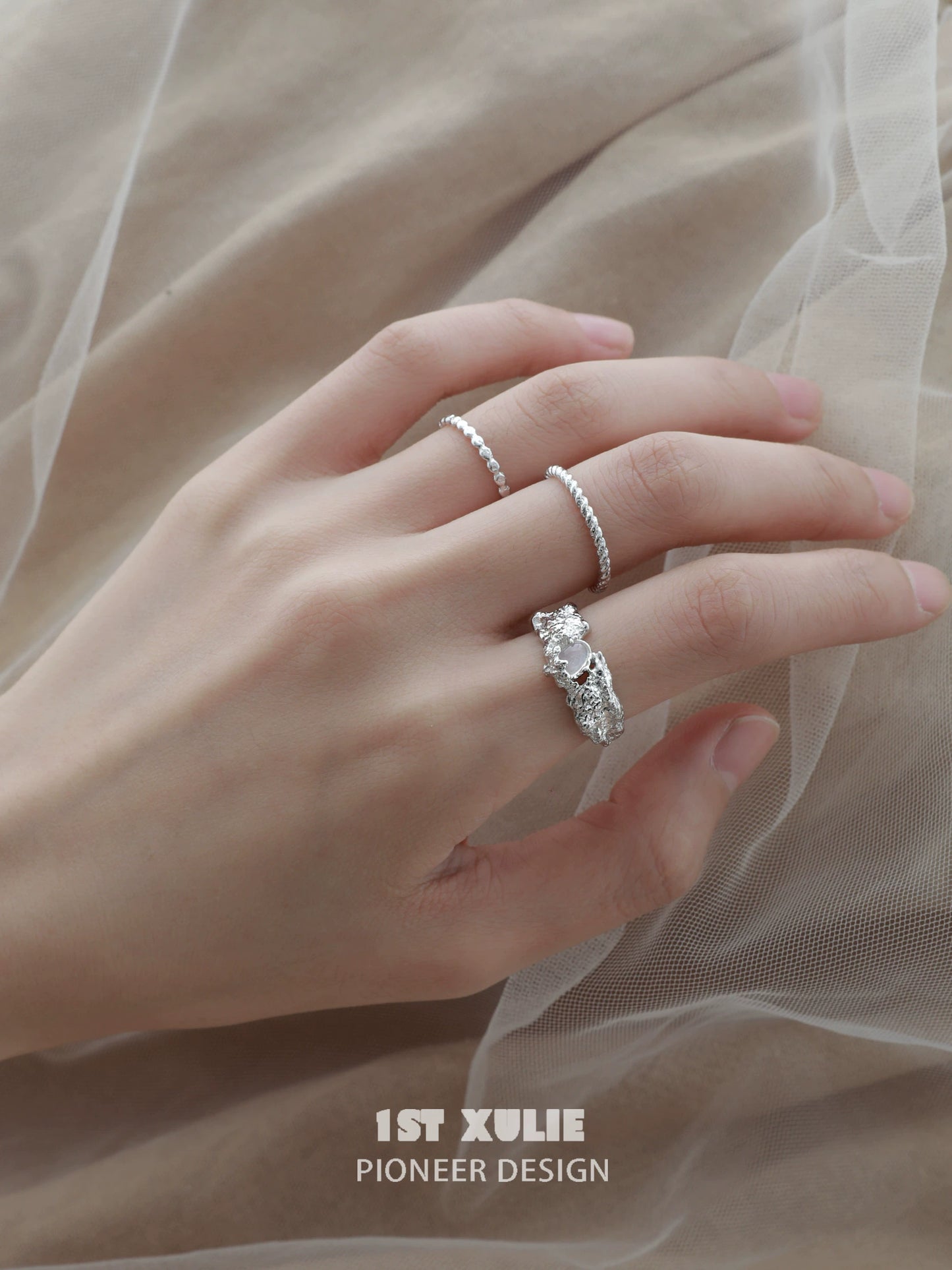Elegant hand wearing a white agate ring alongside two delicate silver bands