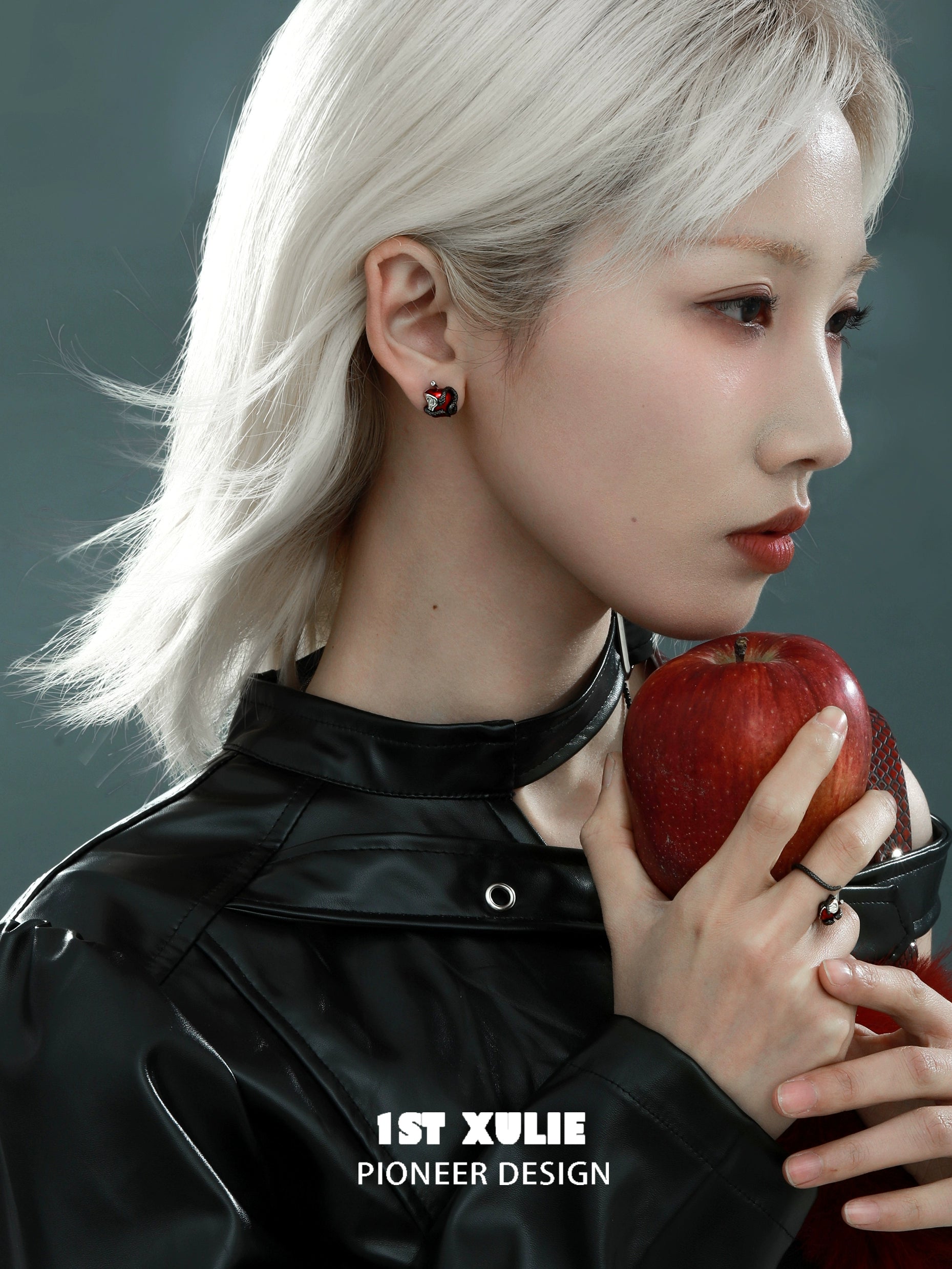 Wicked apple snake ear studs by 1STXULIE showcased on a model holding a red apple